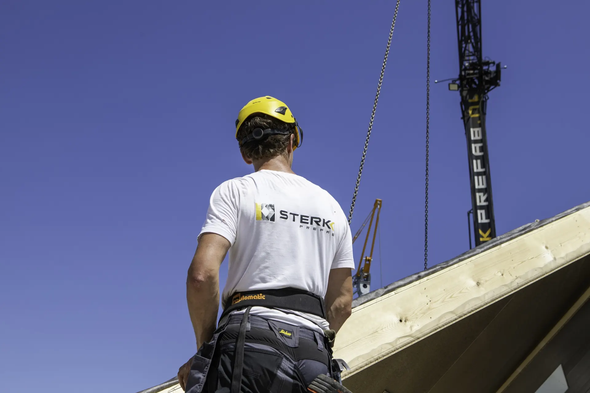 Monteur met Sterkk Prefab-shirt kijkt omhoog naar de kraan