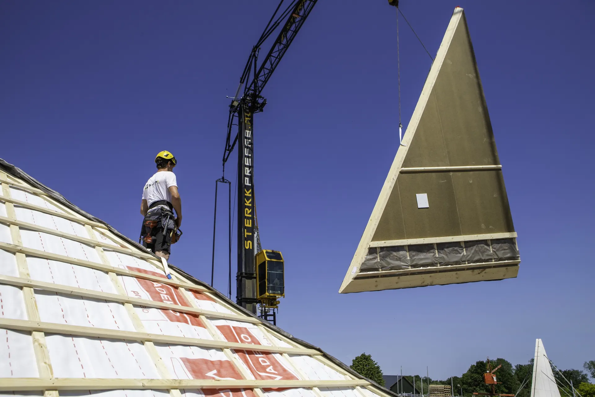 Scharnierkap hangt aan de kraan boven een woning in aanbouw